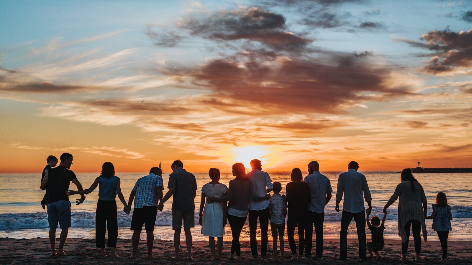 Una familia tomada de la mano frente al atardecer en la playa